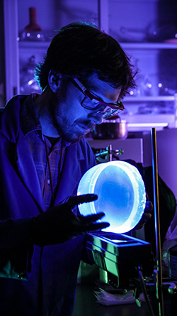 Nick Myllenbeck, a materials scientist at Sandia National Laboratories, examines glowing plastic used to detect radioactive material. (Photo by Lloyd Wilson) Click on the thumbnail for a high-resolution image.
