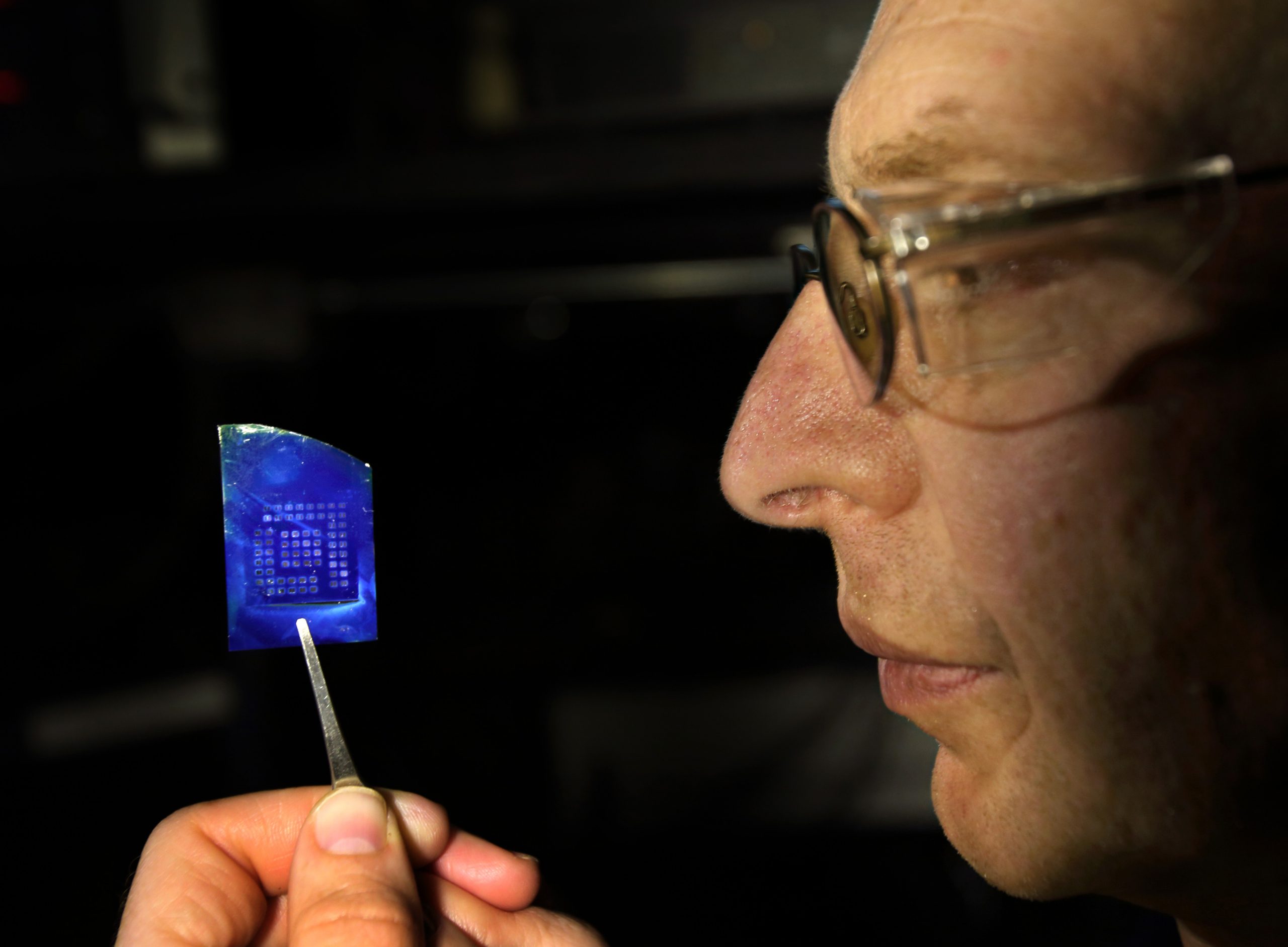 Sandia National Laboratories' Alec Talin inspects a silicon chip coated with a thin oxide layer, an array of platinum electrodes and a MOF film. Optical absorption and interference in the MOF and silicon-dioxide layers give rise to the deep blue color.