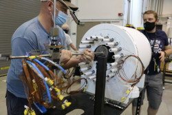 Two men moving a large, white cylinder with wires and tubes sticking out.