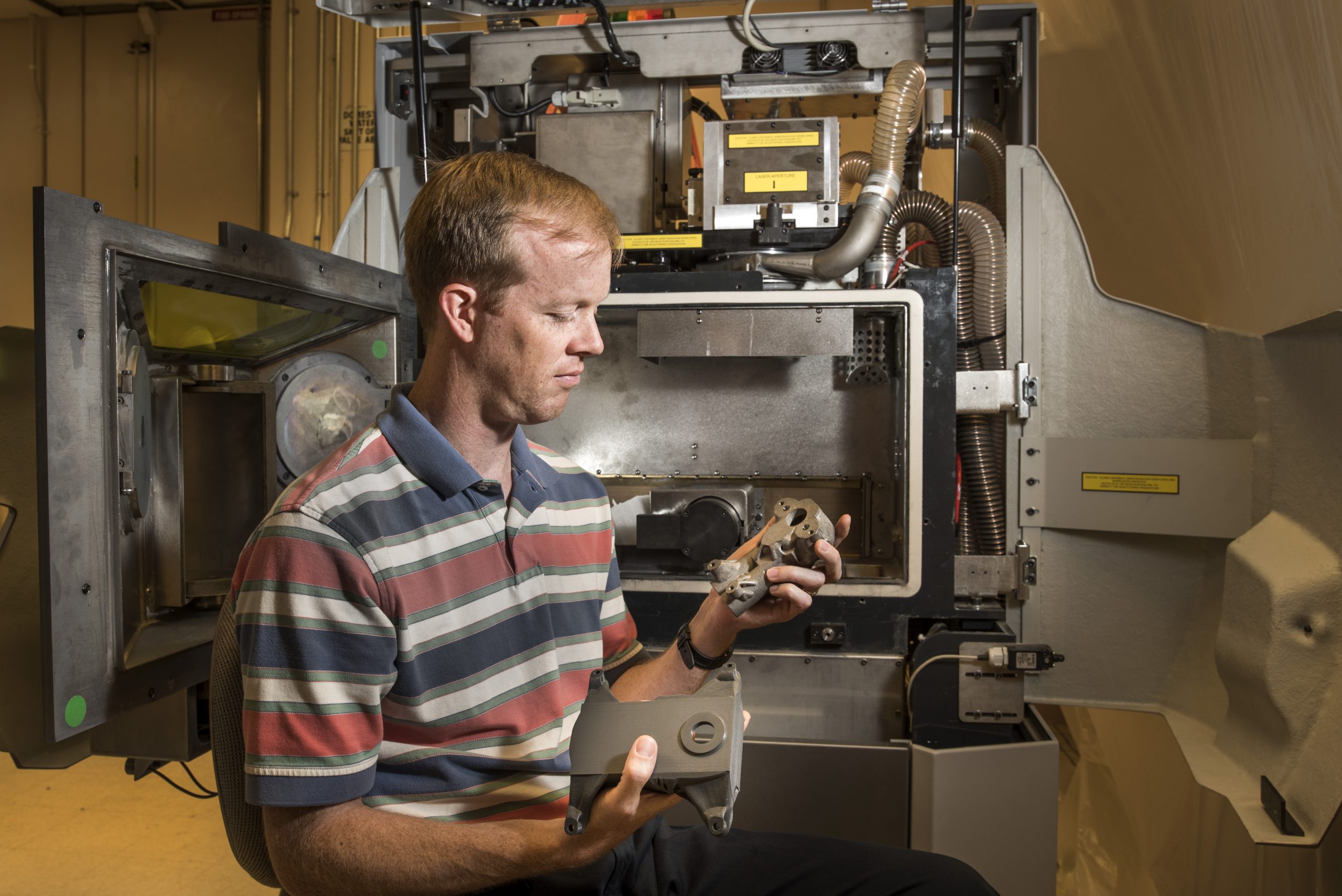 Sandia National Laboratories researcher Bradley Jared sits in front of a new selective laser melting machine at Sandia for metal additive manufacturing as he holds two prototype housings designed through a technology called topology optimization. Sandia researchers who are exploring additive manufacturing for nuclear weapons and other national security needs say they need to understand how additive manufacturing processes affect the properties of materials that are generated.
