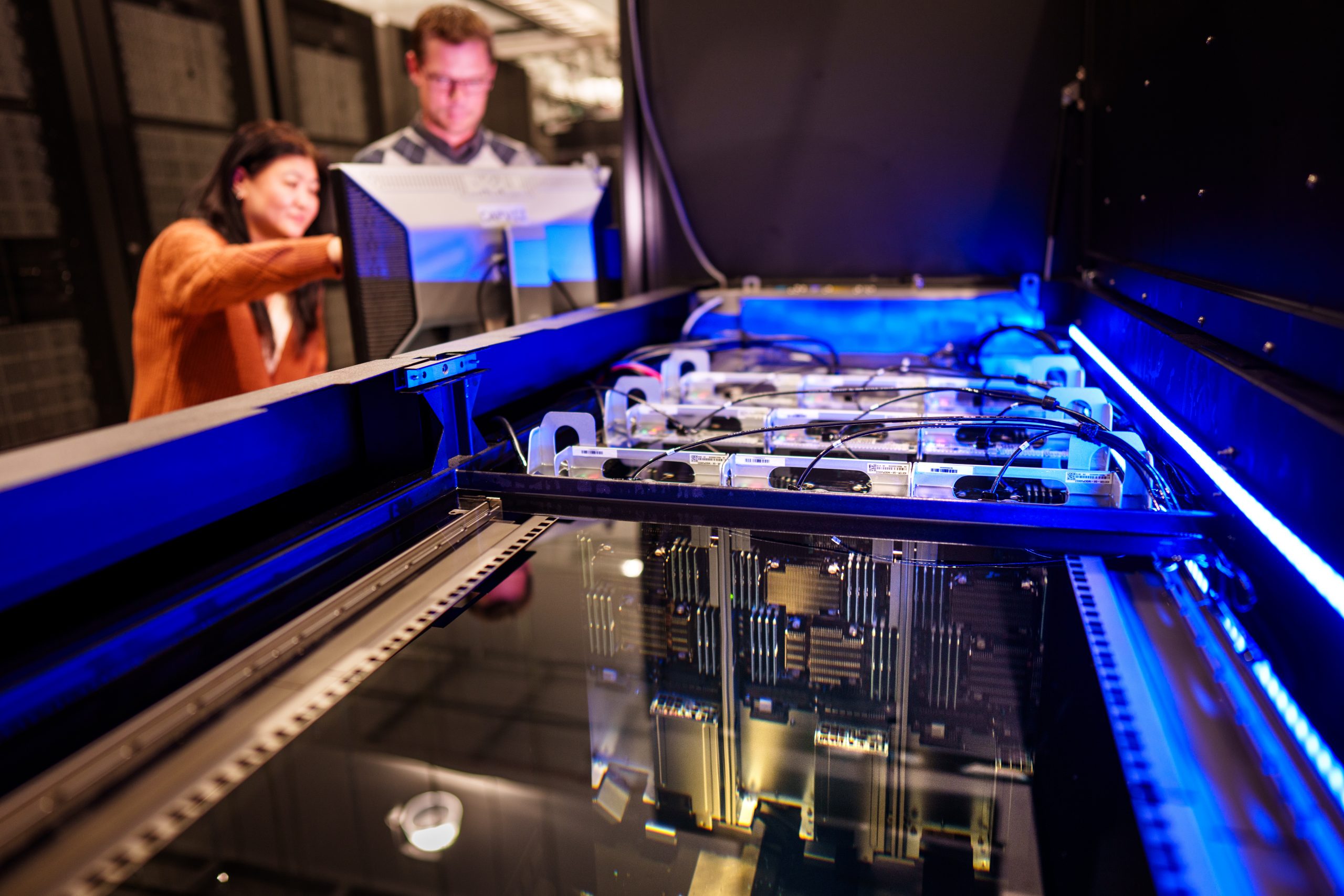 Hoan Luu, left, and David Damm works on a computer server submerged in liquid as part of testing at the High Performance Computing center at Sandia National Laboratories. The immersion system uses a non-conductive liquid coolant which enables 100% of the heat generated to be captured. Save for the silver handles at the top, all is under liquid.
