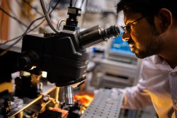 Sandia National Laboratories scientist Ashok Kodigala aligns a fiber to a chip-scale, heterogeneously integrated laser under a microscope at the MESA complex.