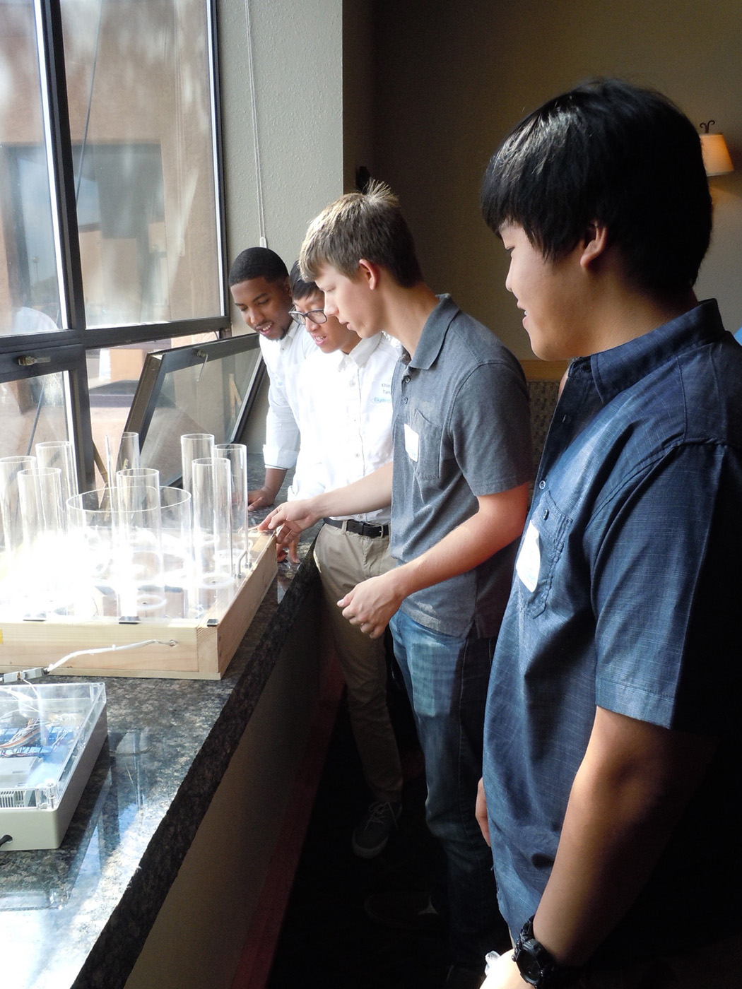 Logan Carpenter, left, designs hardware for cybersecurity training software with fellow interns at Sandia National Laboratories in 2016. Plastic tubes filled with water as software users completed tasks, showing the relative scores of different teams.