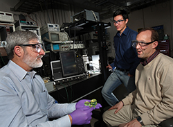 Sandia National Laboratories researcher Patrick Doty, left, holds a few examples of Triplet-Harvesting Plastic Scintillators in his gloved hand, as lead investigator Patrick Feng, center, and Mark Allendorf contemplate their achievement.