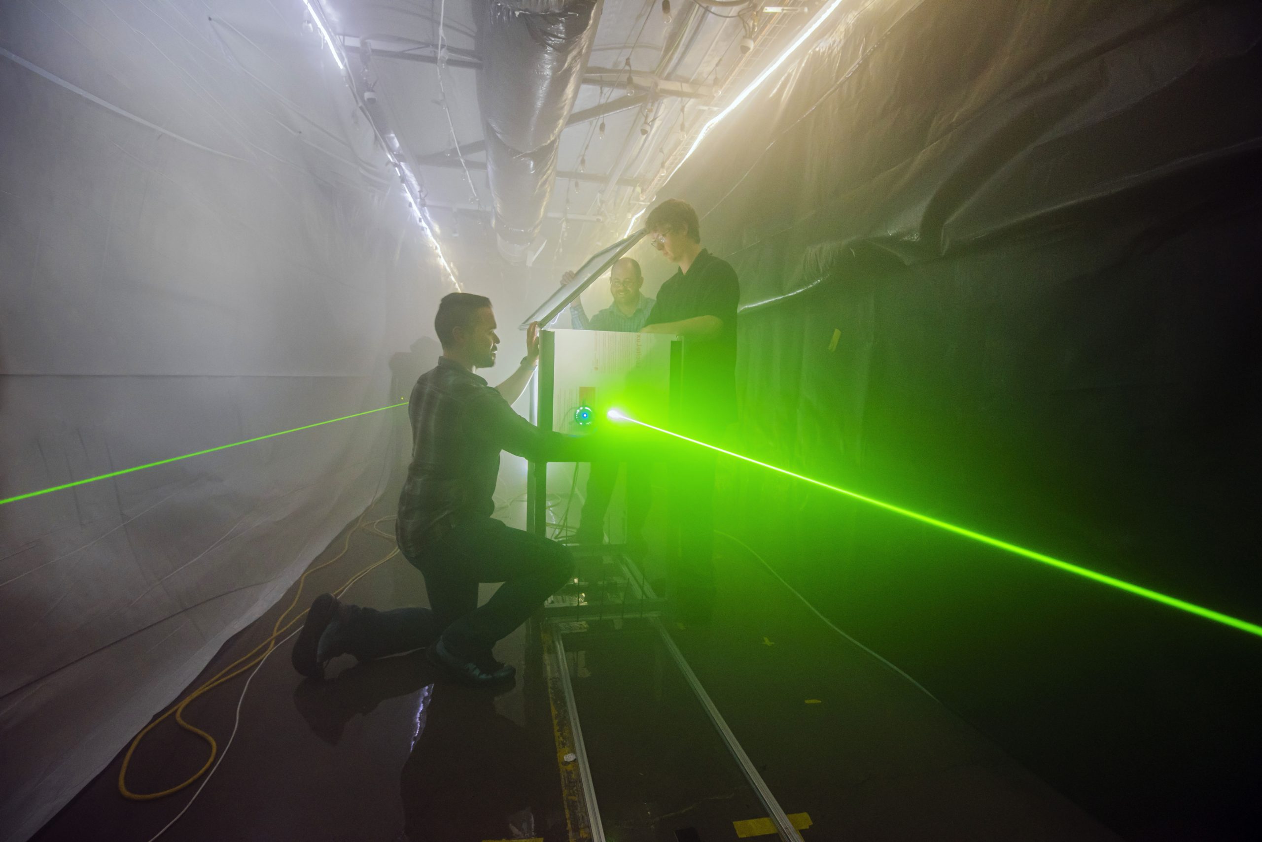 Andres Sanchez, left, Jeremy Wright, center, and Brian Bentz prepare for an optical test in Sandia National Laboratories’ fog facility. Bentz is leading a three-year project to use computational imaging to detect, locate and image objects in fog. This photo was taken prior to the COVID-19 pandemic.