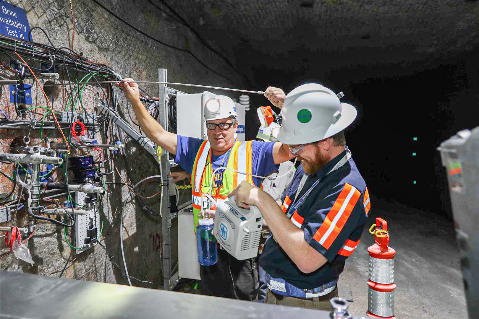 Kristopher Kuhlman, front, a Sandia National Laboratories geoscientist, and Thom Rahn, a Los Alamos National Laboratory scientist, carefully extract a sample of brine from one of the boreholes.