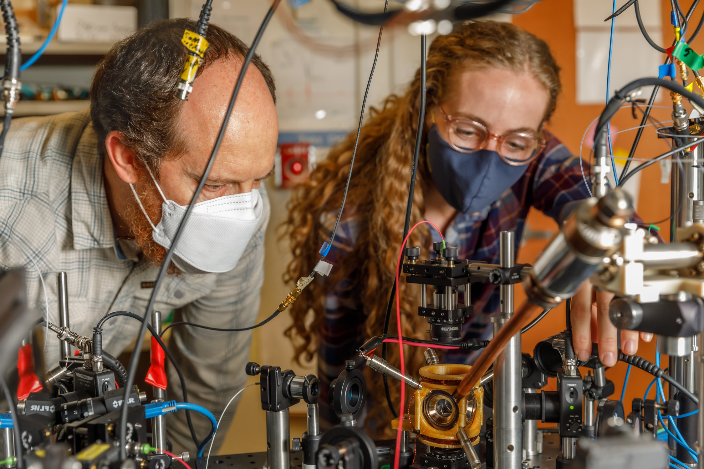 Sandia National Laboratories scientist Peter Schwindt, left, and postdoctoral scientist Bethany Little examine the vacuum package held in a yellow, 3D-printed mount.