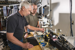 Tom Crenshaw, left, of Sandia National Laboratories mounts a small shape memory alloy sample into a hydraulic test frame for mechanical testing while Tom Buchheit looks on. Sandia researchers are creating high-temperature shape memory alloys.