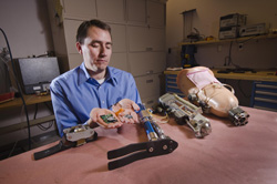 Robotics engineer Steve Buerger displays implantable and wearable neural interface electronics developed by Sandia as he sits in the prosthetics lab with a display of prosthetic components. He is part of a research team that is working on ways to improve amputees’ control over prosthetics with direct help from their own nervous system.