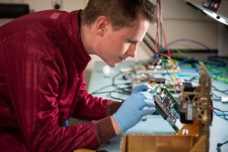 Thomas Bradshaw, electrical engineer and flight software lead, inspects a computer board for an upcoming remote sensing mission designed to demonstrate next-generation high-performance computing in space. The team used Valhalla, a Python-based high-performance computing program developed at Sandia National Laboratories, to quickly generate the concept design and estimate mission performance for the payload.