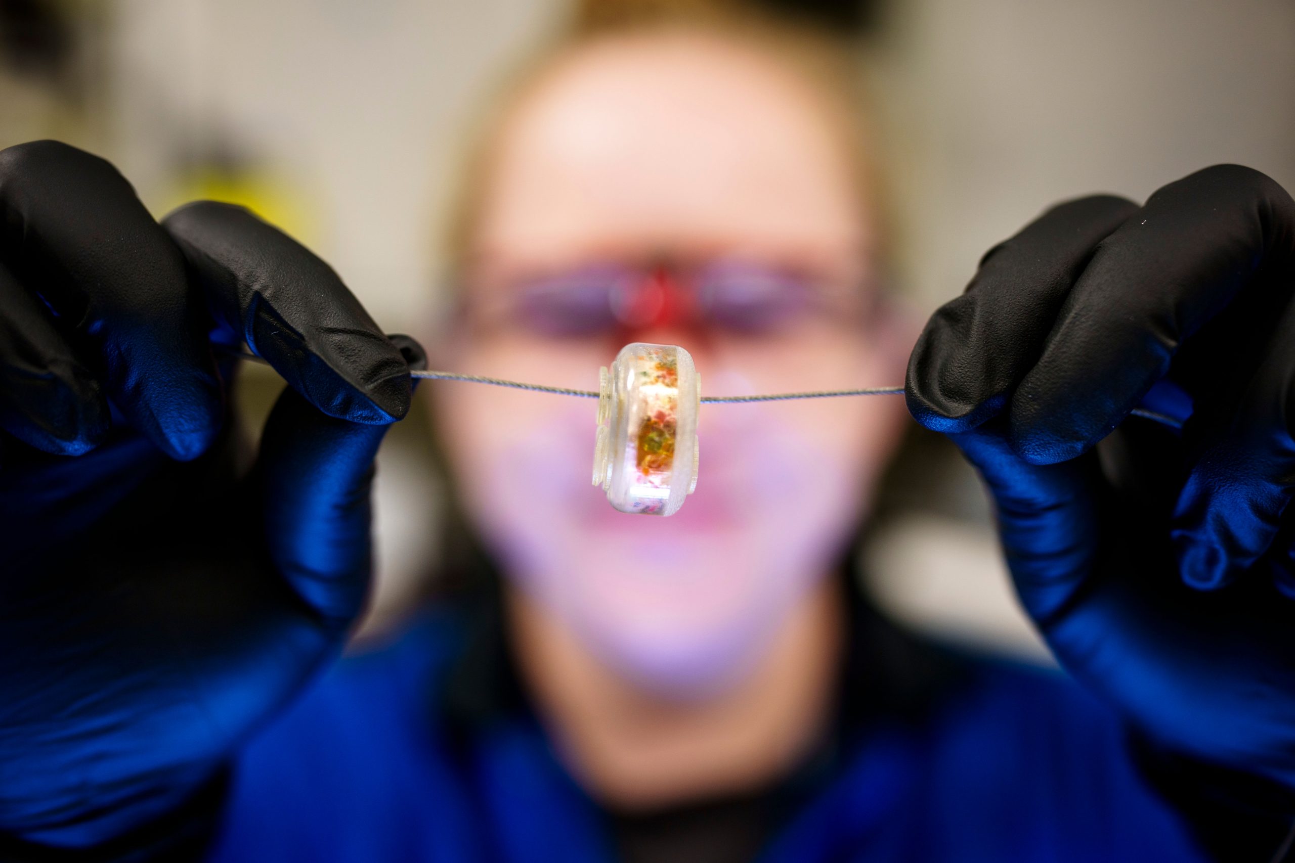 Sandia National Laboratories postdoctoral researcher Stephanie White holds up a prototype tamper-indicating device. The colored speckles make each device near-impossible to counterfeit, while the solution inside turns brown if the casing is cracked or the wire is pulled, indicating attempts to access whatever is behind the device.