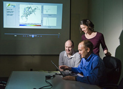 Sean McKenna, seated right, works with Kate Klise, standing, and Dave Hart, left, on the CANARY Event Detection Software, which is open source software developed by Sandia in partnership with the Environmental Protection Agency to enhance the detection of terrorist attacks or natural contaminants to public drinking water systems. The projected image shows what a utility operator might see, including a map locating a sensor that has detected contamination, a graph