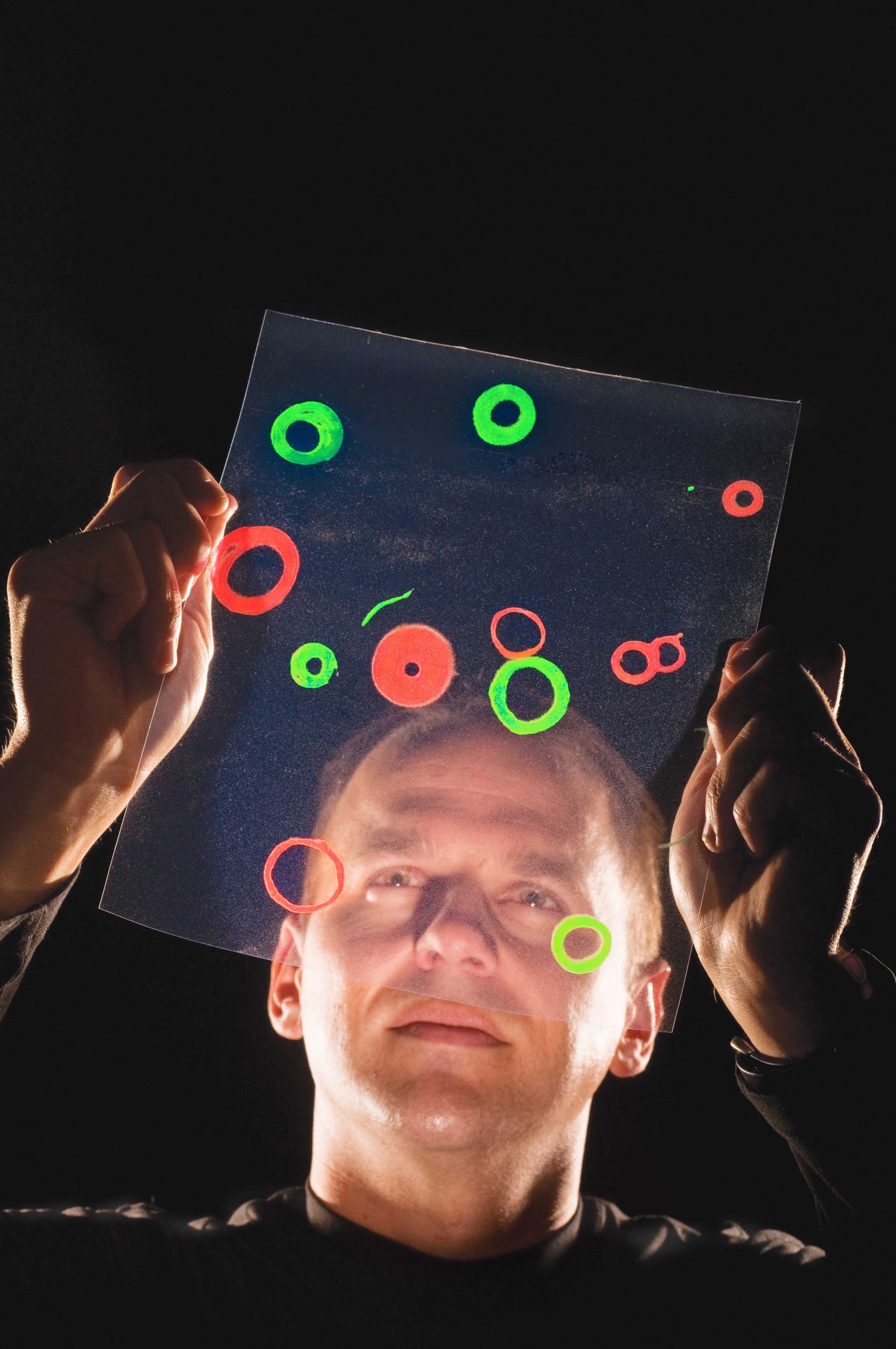 TRUE TO LIFE--Sandia researcher George Bachand examines an enlargement of actual images of light-emitting quantum dots. These ride microtubules that have spontaneously formed stable circles of about 5 microns diameter. The picture superimposes two separate images – one of green rings and one of red – for visual effect. The images were processed to remove noise and maximize contrast. <br />
