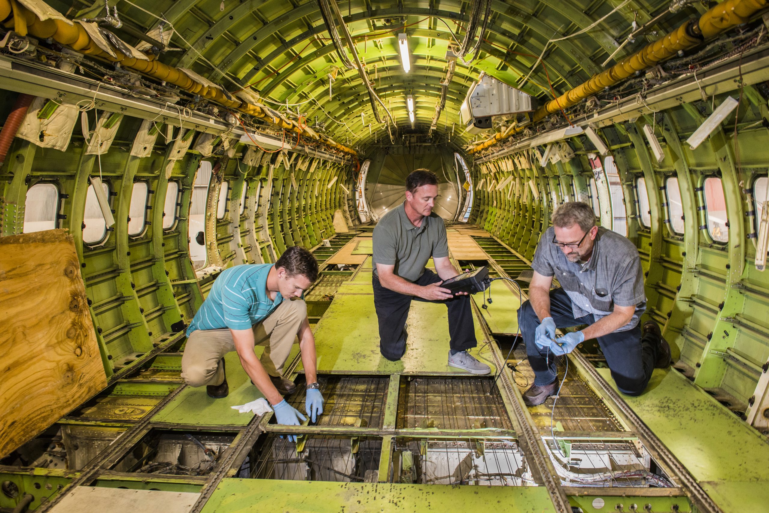 Sandia National Laboratories senior scientist Dennis Roach, center, works inside the cabin of a B737 test bed, installing and acquiring data from Structural Health Monitoring sensors with Sandia mechanical engineers Stephen Neidigk and Tom Rice.