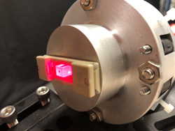 This laser-illuminated crystal, less than a half-inch long, is supported by a free-standing retaining structure with no physical connection to Sandia National Laboratories' HERMES accelerator cathode. In the actual experiment, the light is initially extinguished by crossed polarizers. When the accelerator fires, the polarized light is rotated so that it leaks through the second polarizer. The leaked amount is directly proportional to the electric field.