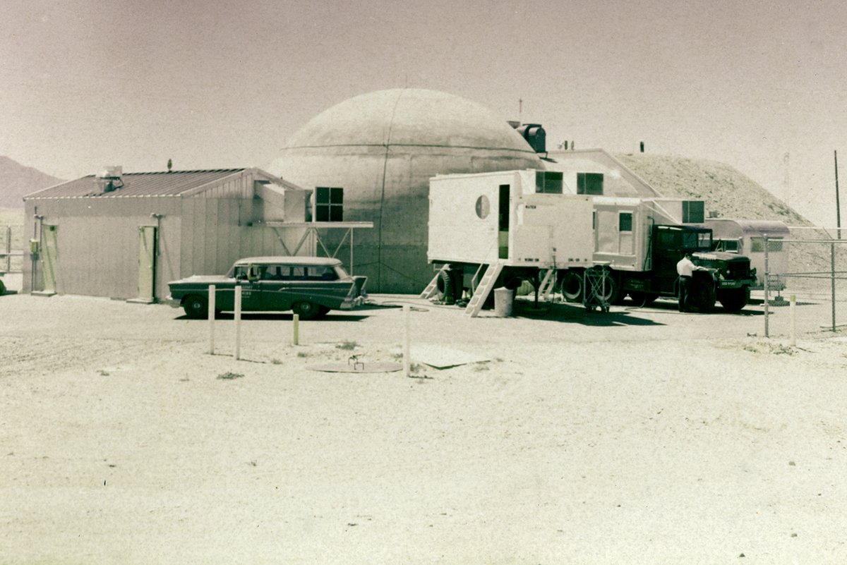 This photo, taken in the early 1960s, shows the reactor building and the original instrumentation building. The domed structure is the Reactor building, called the Kiva, and the metal building next to the Chevy Nomad is the Instrumentation Building.