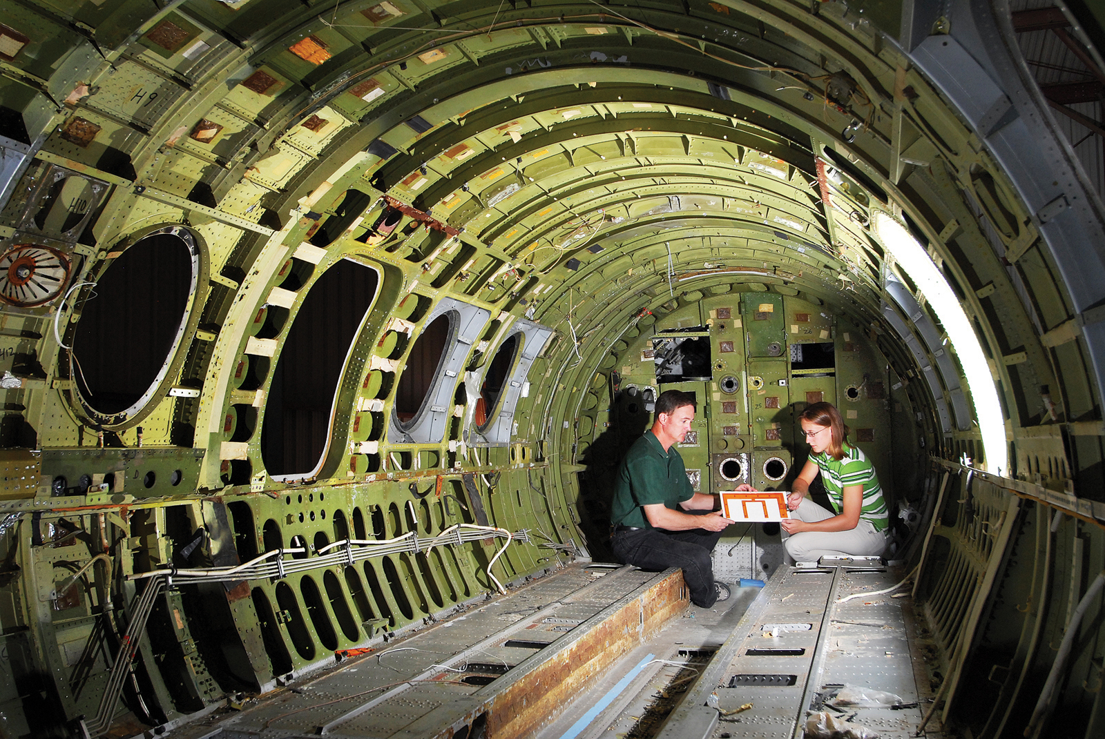 In the back of a commuter jet used as a testbed at Sandia, Dennis Roach and Ciji Nelson examine piezoelectric sensors placed on a printed circuit board for mounting to an aircraft structure. (Photo by Randy Montoya)