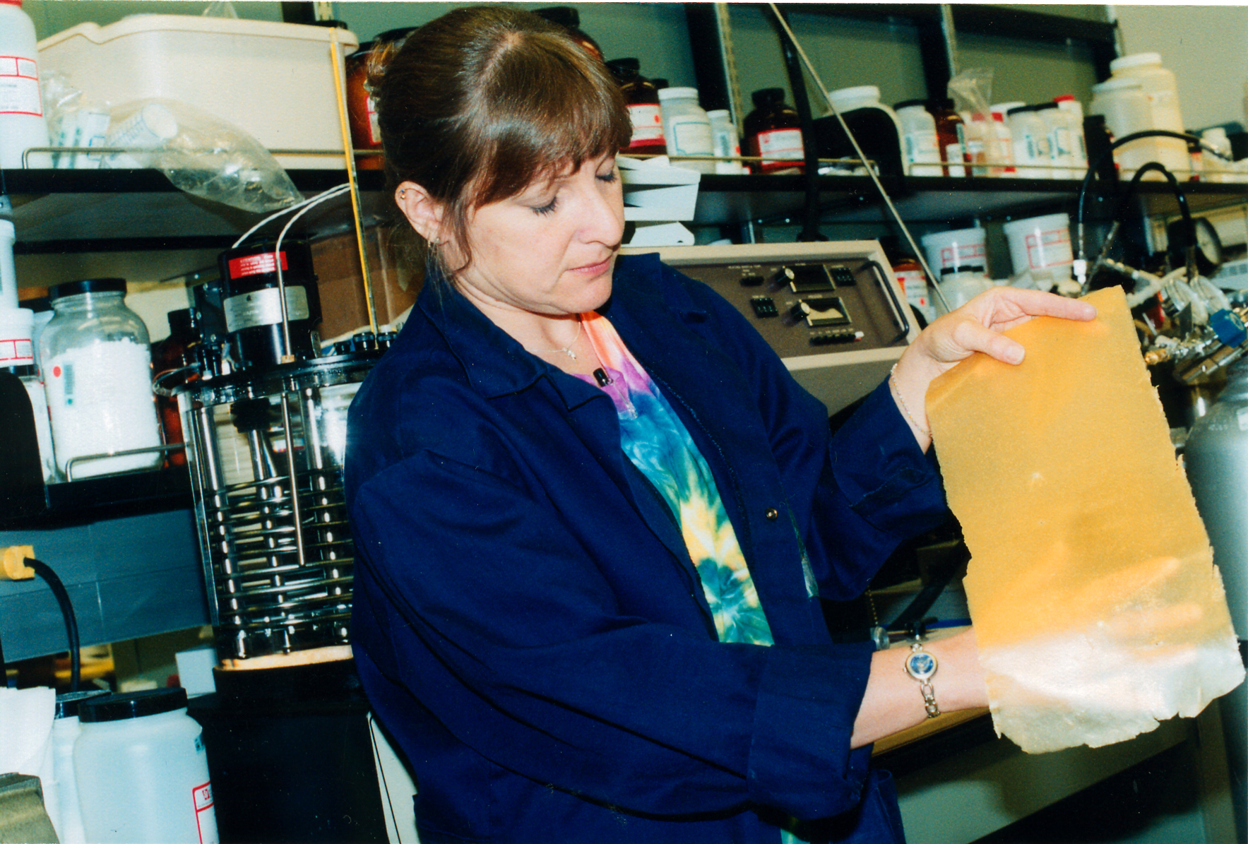 REMOVABLE ADHESIVE — Sandia technologist Patti Sawyer holds a sheet of unheated adhesive developed by Jim Aubert. In the unheated state, it looks and feels like a rubber band. No other adhesive with the strong bonding characteristics of an epoxy can melt and lose its bonding capability at high temperatures and then rebond when the temperature is lowered.