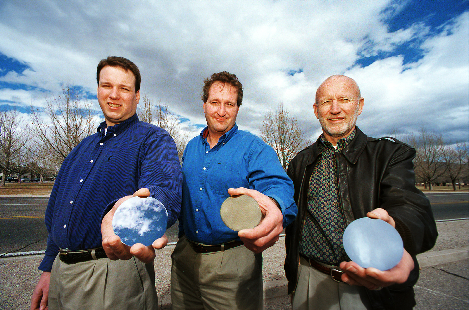 CRAZY PHYSICS GOING ON -- Researchers at Sandia National Laboratories, from left, Normand Modine, Andy Allerman, and Eric Jones display wafers made of the new semiconductor alloy, indium gallium arsenide nitride (InGaAsN). They are developing it for possible use as a photovoltaic power source for space communications satellites.