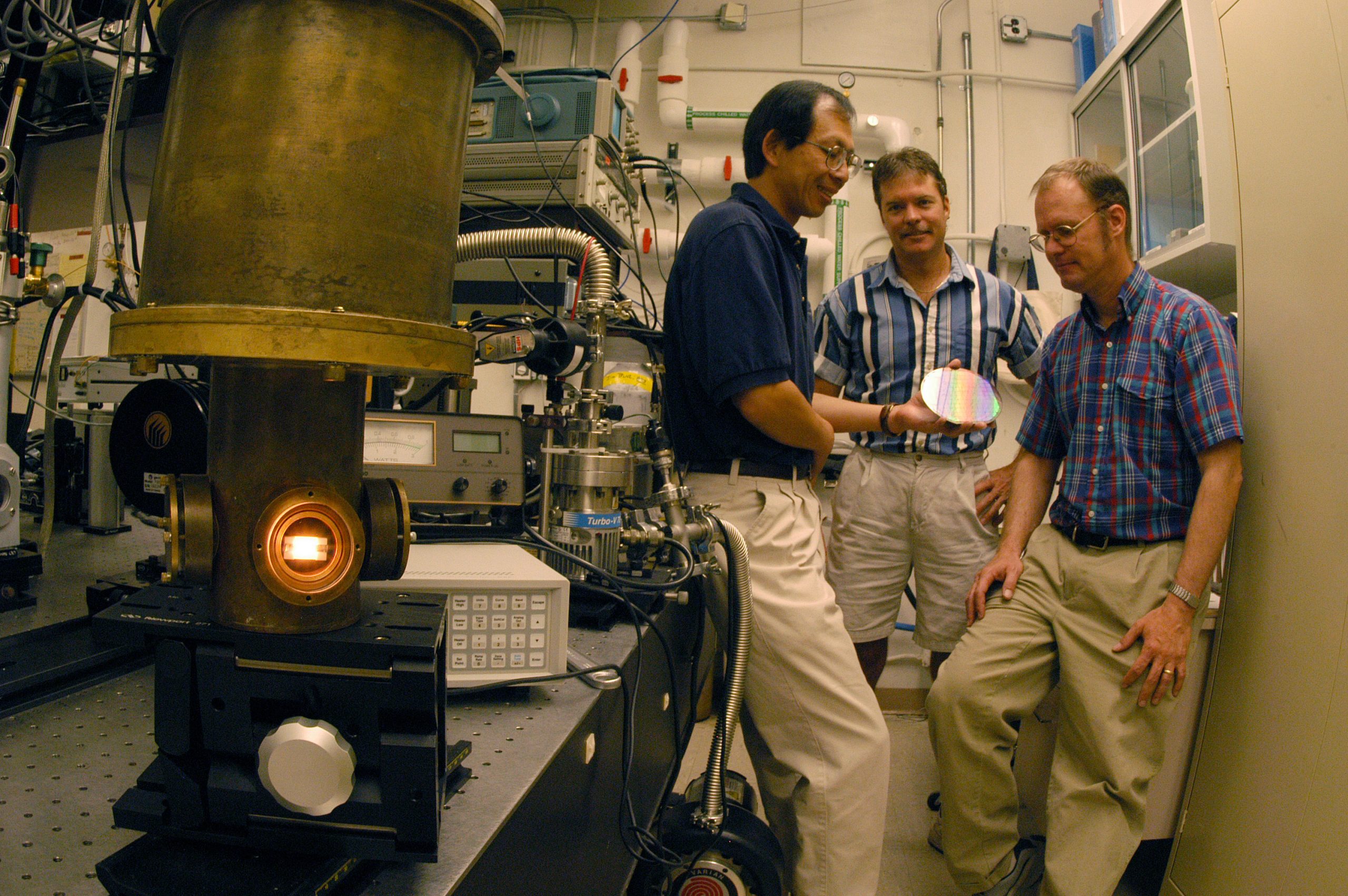 WATCH OUT, IT’S LIVE: from left, Sandians Shawn Lin, Jim Bur, and Jim Fleming discuss the possibilities of tungsten photonic lattices as one, electrically driven, glows in the left foreground. (Photo by Randy Montoya)