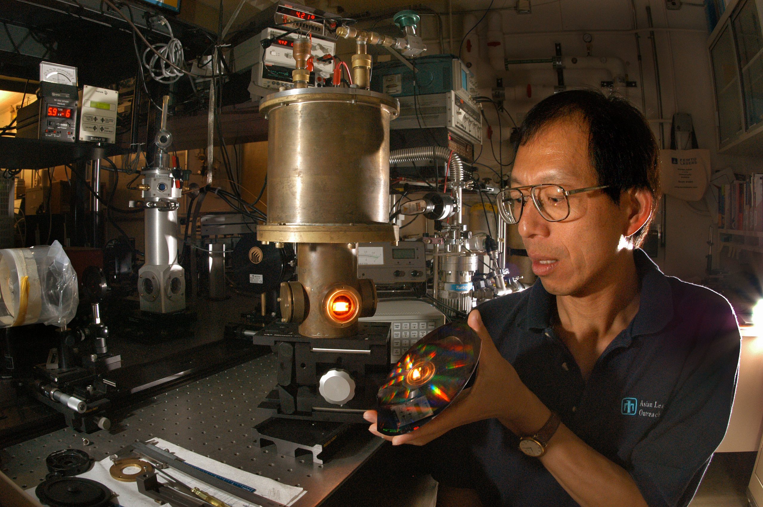 THE REAL HARRY POTTER? — A tungsten photonic lattice glows in a vacuum chamber as Sandia researcher Shawn Lin inspects an iridescent disk that contains approximately 1,000 tungsten photonic lattices. Most emissions from these filaments are in the near-infrared range, and may improve efficiencies of heat-driven engines like hybrid electric automobiles. (Photo by Randy Montoya)