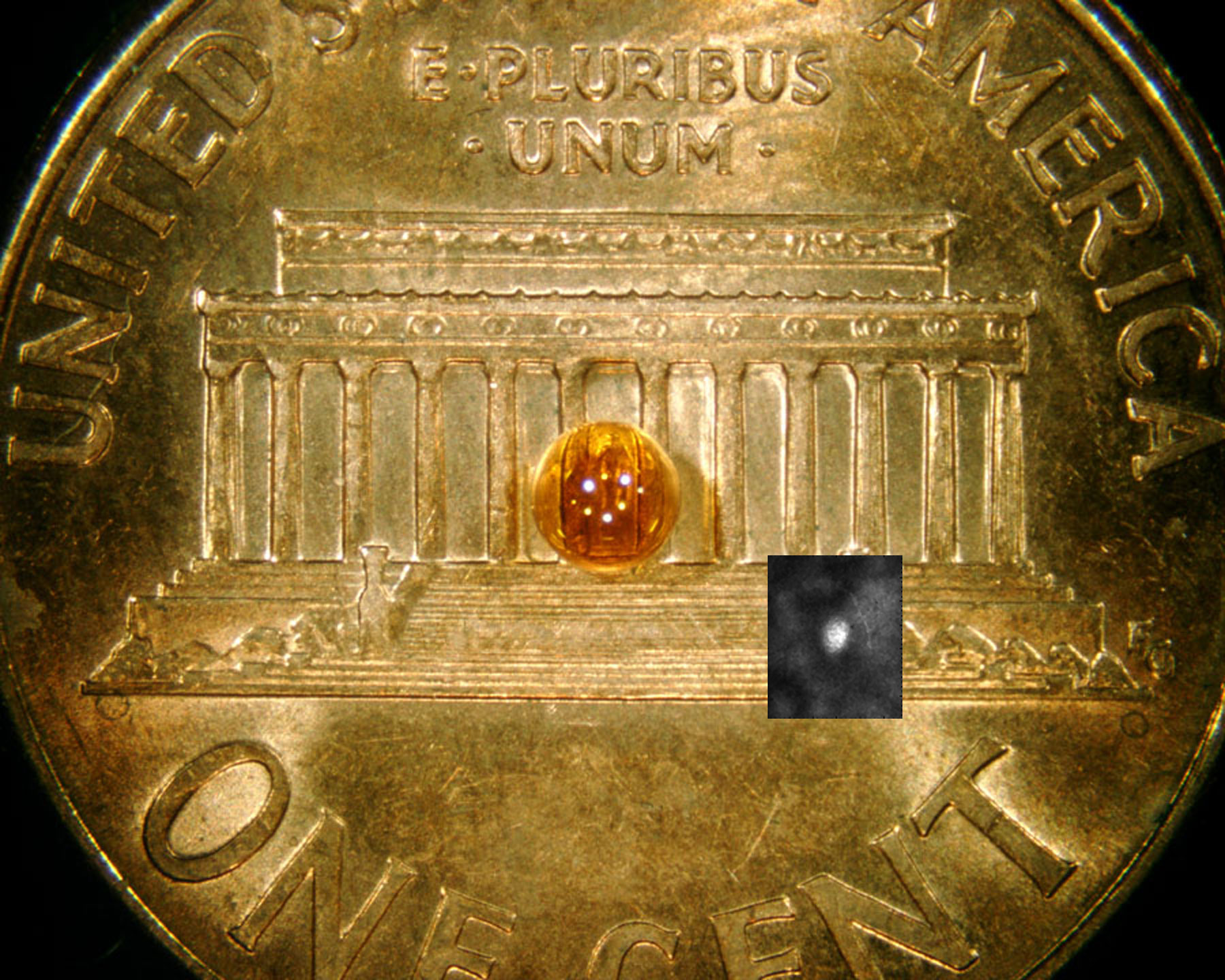 A 2 mm. plastic capsule shell sits atop a Lincoln penny with an inset of an X-ray image from the hot, imploded capsule. The smaller bright image of the X-ray core is consistent with a 7X reduction in size through the implosion process. Photo by Diana Schroen.