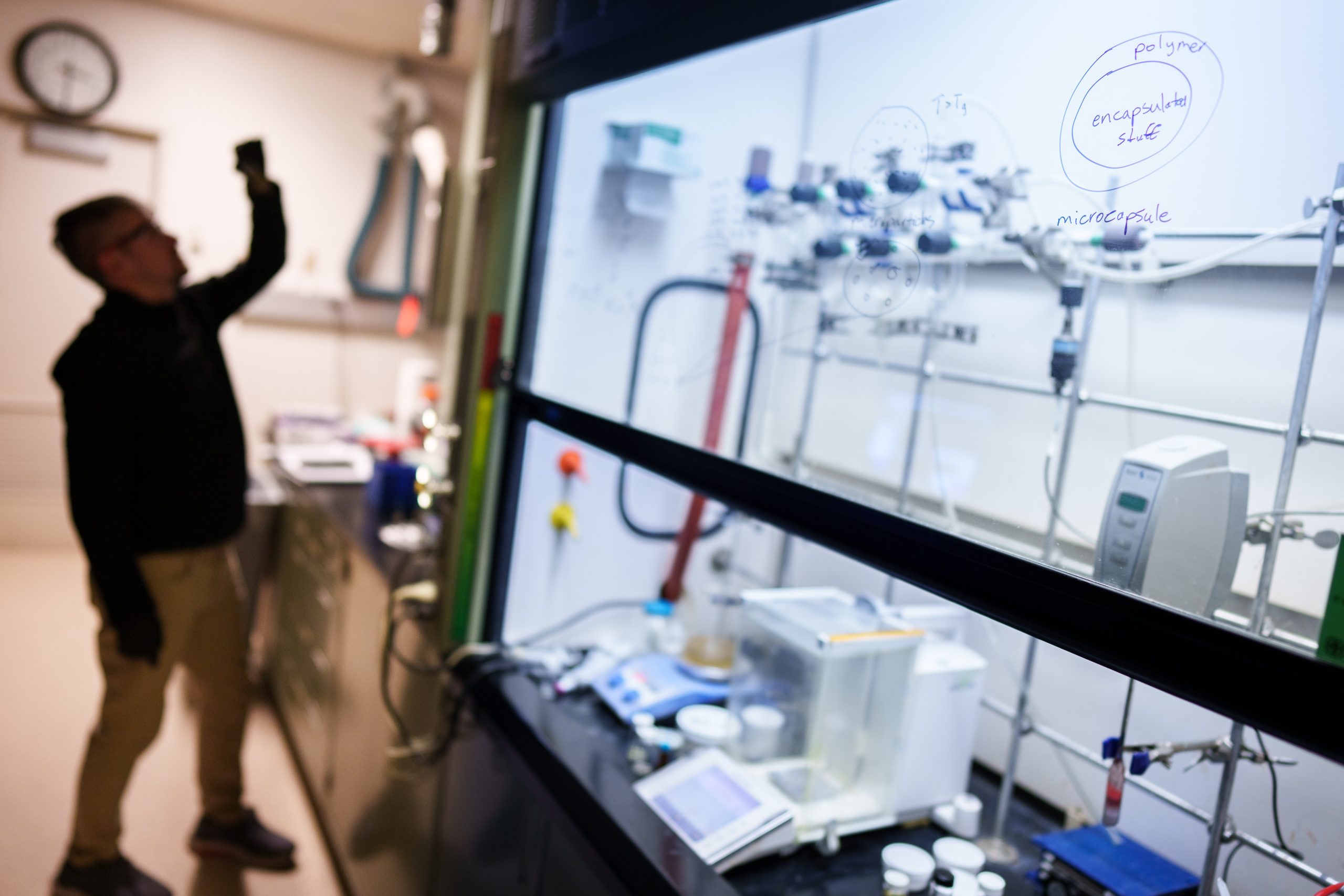 Oleg Davydovich prepares a resin that can be polymerized on-demand as part of microencapsulation technology developed at Sandia National Laboratories, as demonstrated by the diagram on the hood sash. 