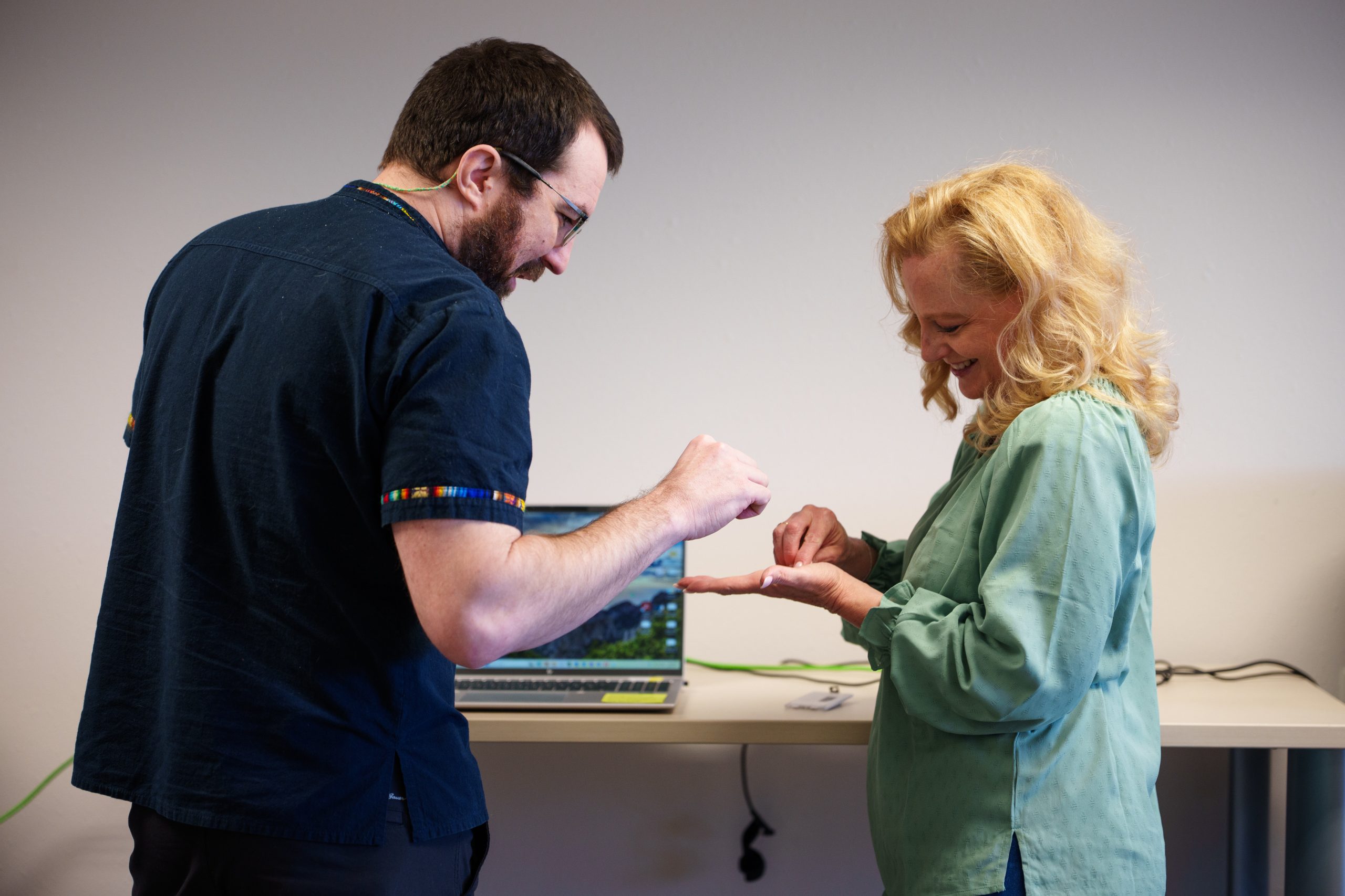A man and a woman stand beside a laptop, looking at a tiny item in the woman's hand.