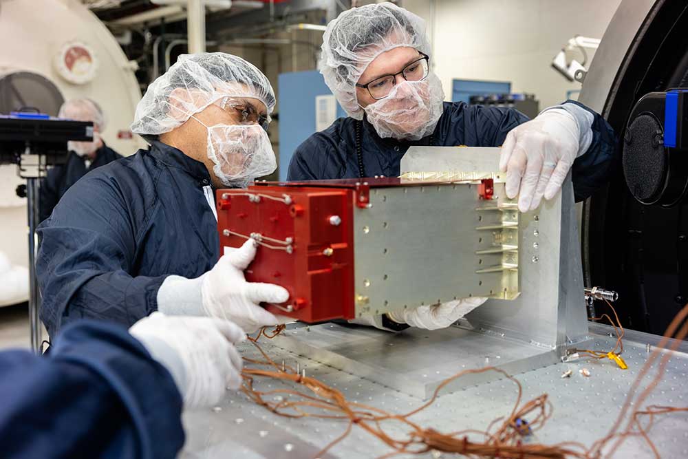 Engineering technologist Adolfo Salazar, left, and systems engineer Sean Walker prepare a sensor from the IIIF Global Burst Detector for thermal vacuum testing. 