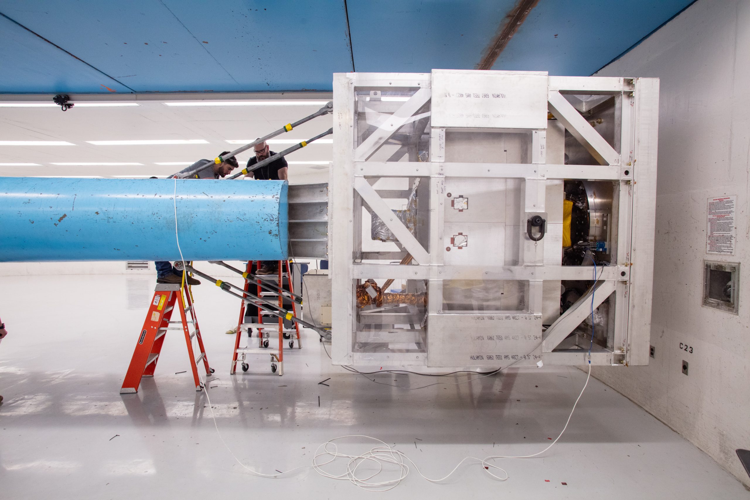Toby Gomez, left, and Jason King work on sensor connections while the VIPER rover is suspended in a cage at the end of the Superfuge arm at Sandia National Laboratories.