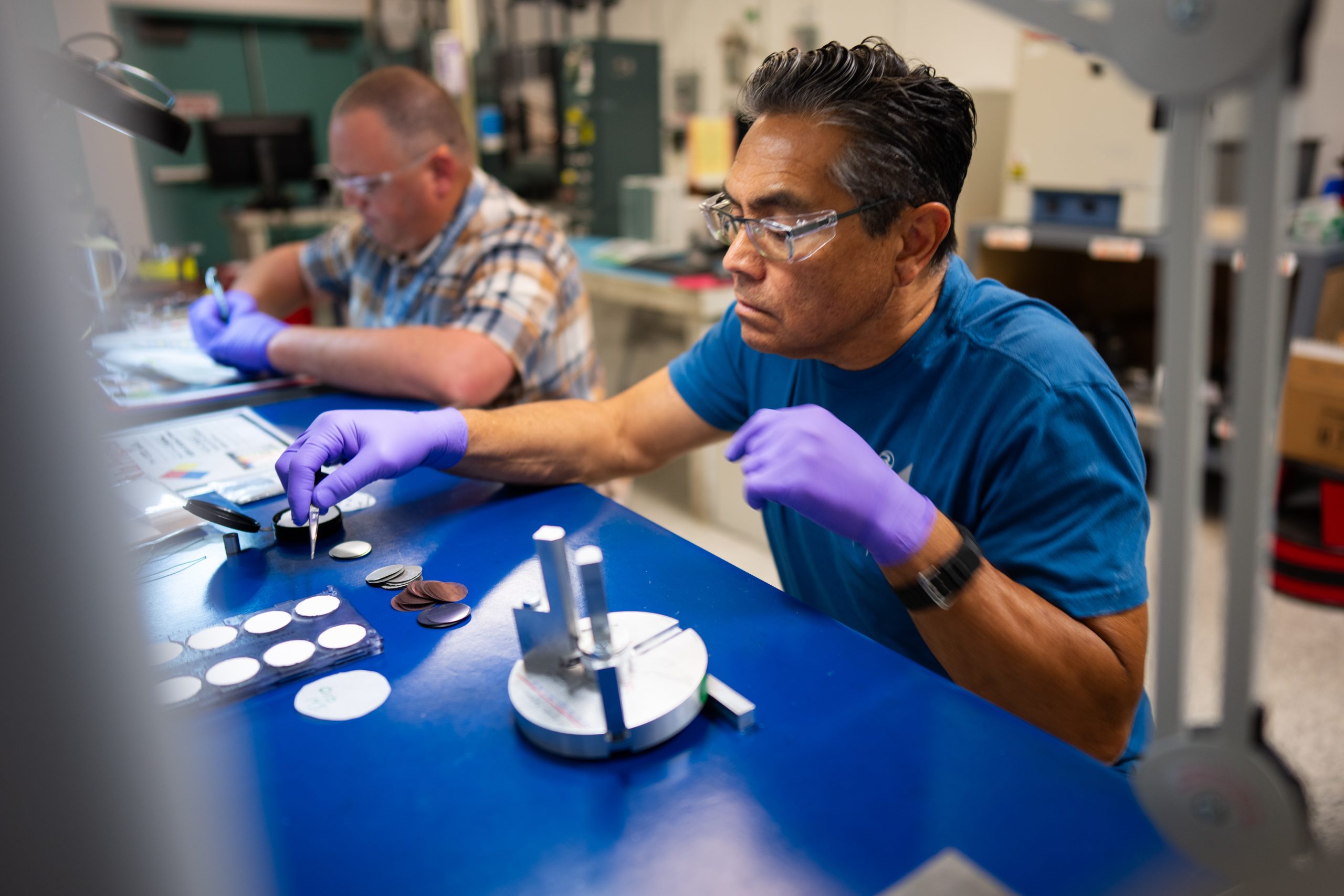 A technologist at Sandia National Laboratories works on a thin film thermal battery as his colleague performs quality assurance checks for the Power Sources Capabilities team. 