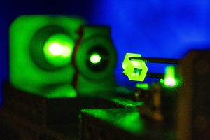 A green light shining through several objects, illuminating a small rectangular crystal.