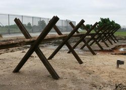 This type of surface-mounted vehicle barrier is currently  deployed by Customs and Border Protection (CBP) in the southwest U.S. border region. The design style involves used railroad rails that are  welded into the crossed X configurations, and a continuous rail section is welded across them.
