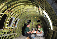 In the back of a commuter jet used as a testbed at Sandia, Dennis Roach and Ciji Nelson examine piezoelectric sensors placed on a printed circuit board for mounting to an aircraft structure