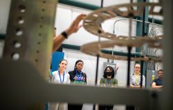 Four college students observe while a tour guide touches metal rings at head height.