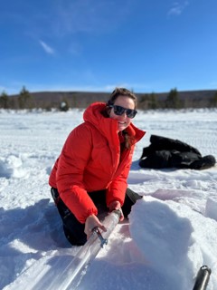 A woman kneeling on ice, with a clear tube, wearing a red coat.