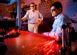 Prasad Iyer, right, and Igal Brener demonstrate optical hardware at Sandia’s CINT facility used for beam steering experiments as a red beam of light is reflected in an arch. 