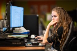 Young woman sitting at a desk, looking at a computer screen. Blurred background.